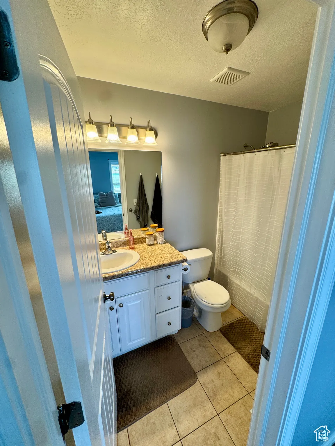 Full bath featuring a textured ceiling, vanity, light tile patterned floors, and connected bathroom