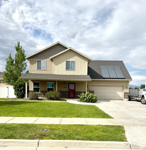View of front facade with covered porch, board and batten siding, roof mounted solar panels, and driveway