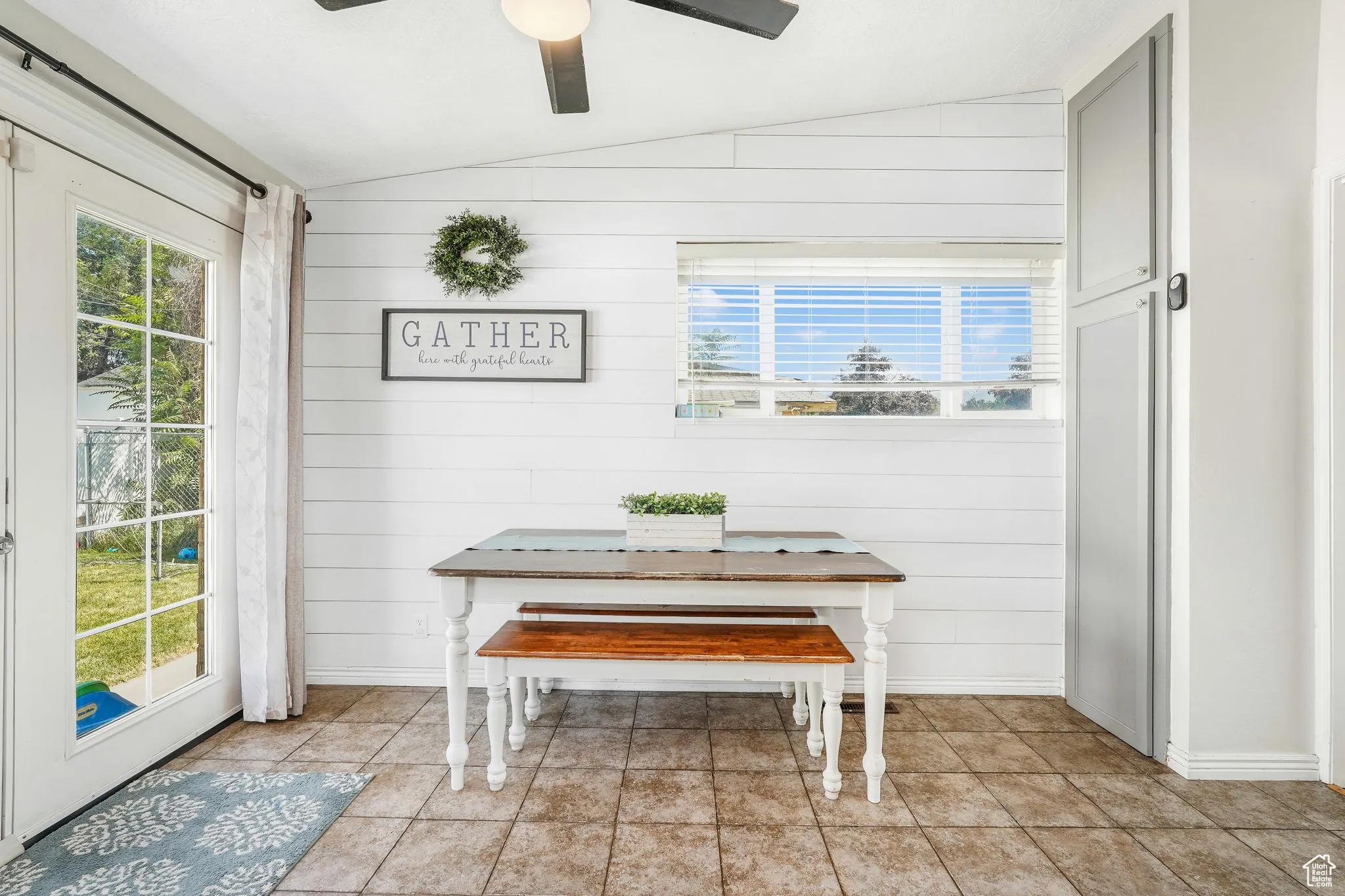 Dining area with lofted ceiling, wood walls, light tile patterned floors, and ceiling fan