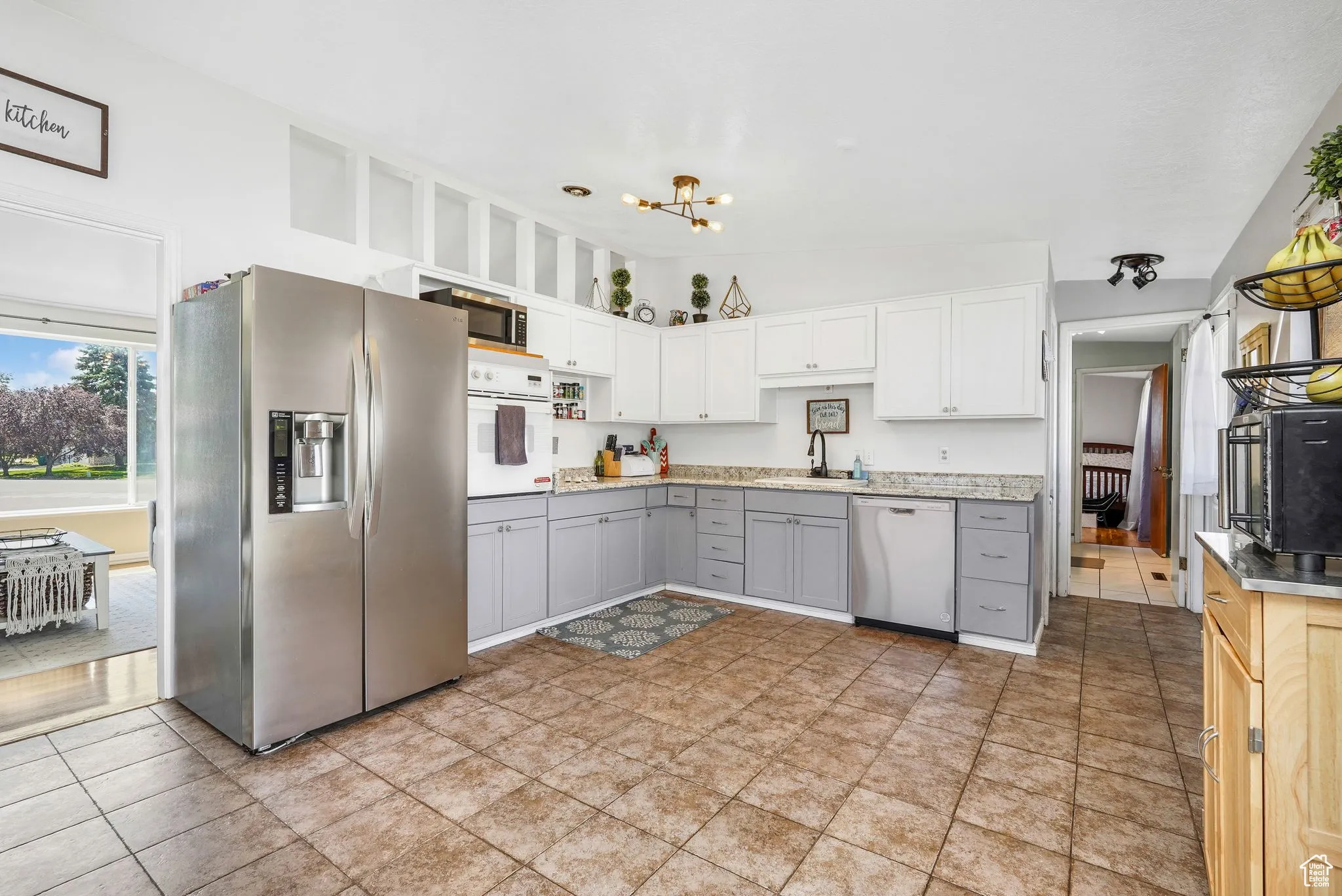 Kitchen featuring appliances with stainless steel finishes, gray cabinetry, a chandelier, white cabinetry, and light tile patterned floors