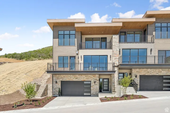 Contemporary house featuring stone siding, a balcony, concrete driveway, and a garage