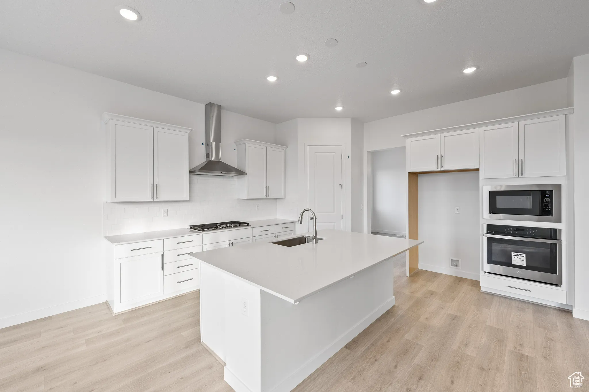 Kitchen featuring appliances with stainless steel finishes, recessed lighting, an island with sink, white cabinets, and light wood-type flooring