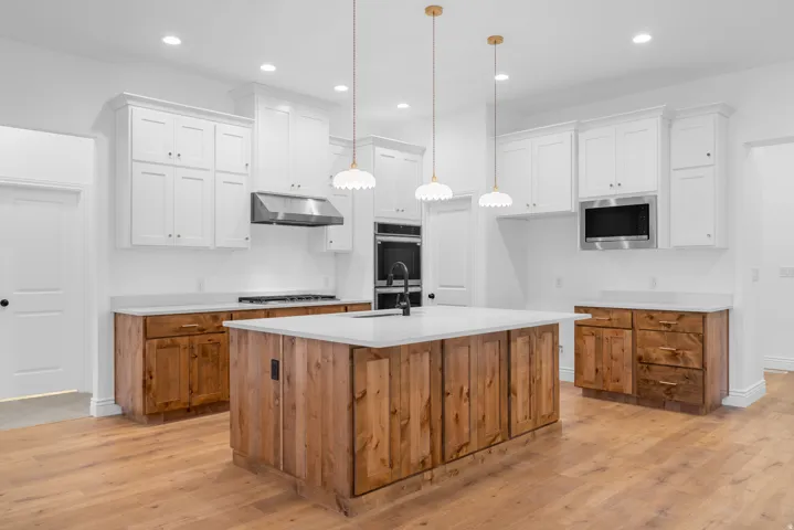 Kitchen featuring two tone cabinetry, an island with sink, light wood-type flooring, stainless steel appliances, and hanging light fixtures