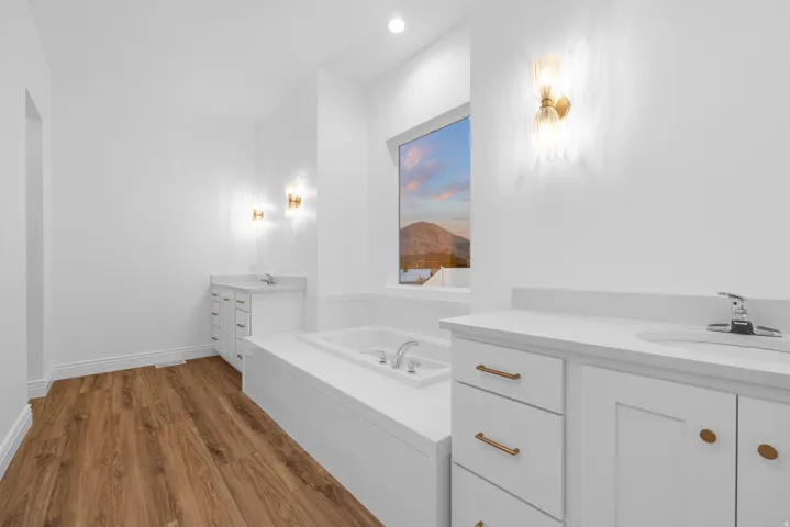 Full bath featuring two vanities, dark wood finished floors, a garden tub, and recessed lighting