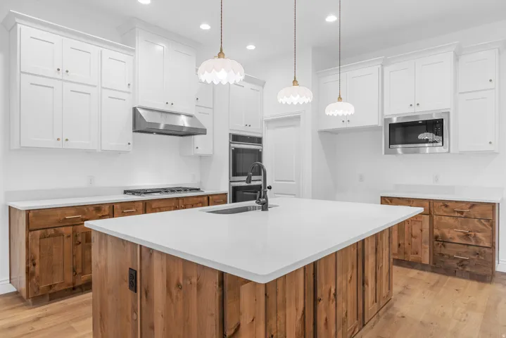 Kitchen featuring an island with sink, light wood finished floors, stainless steel appliances, dual tone cabinetry, and hanging light fixtures