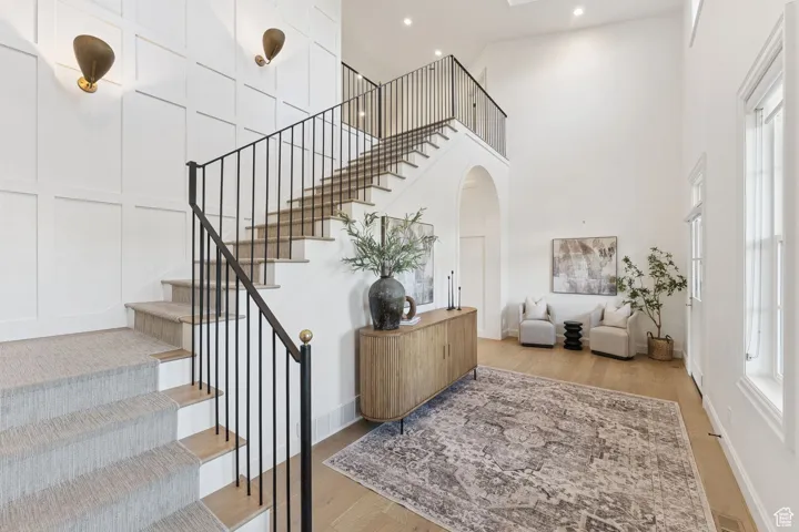 Staircase with a towering ceiling, wood finished floors, arched walkways, and a decorative wall