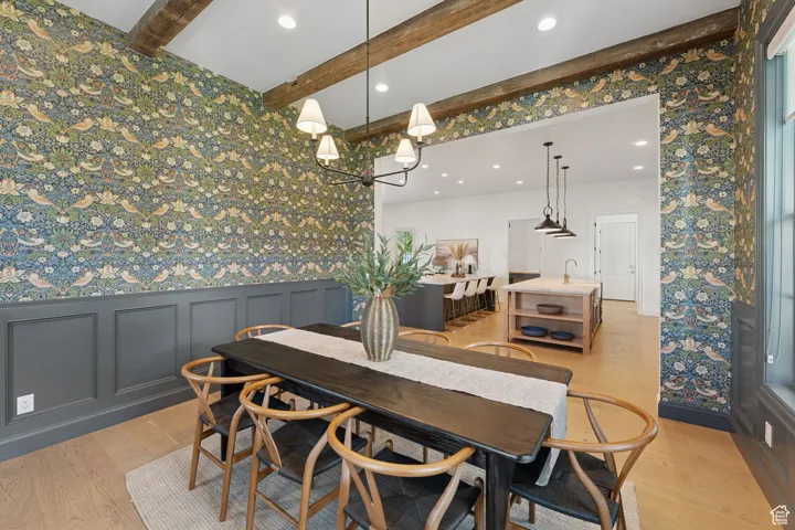 Dining room featuring wallpapered walls, light wood-style flooring, beam ceiling, recessed lighting, and a wainscoted wall