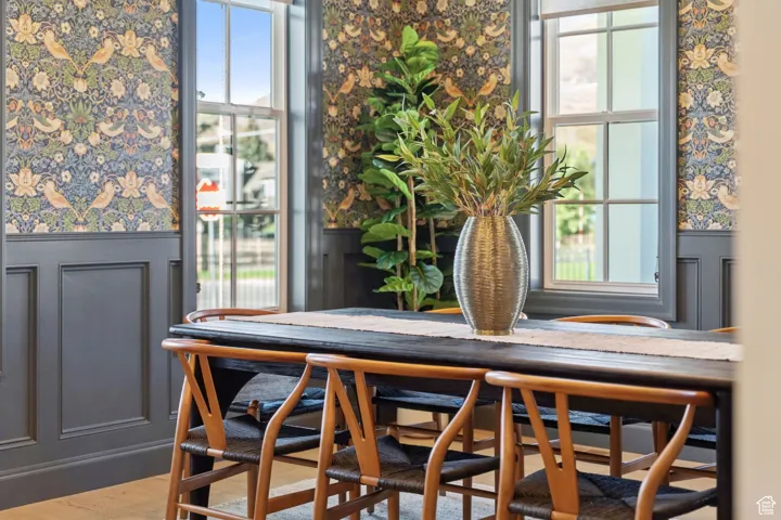 Dining space with wainscoting, a decorative wall, wallpapered walls, and wood finished floors