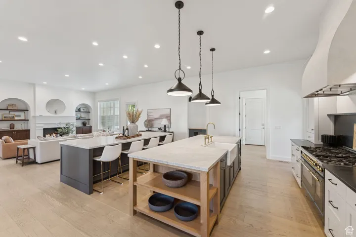Kitchen featuring open floor plan, pendant lighting, open shelves, range with two ovens, and light wood-style flooring