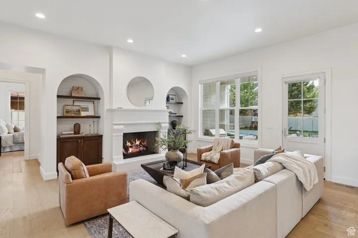 Living area with recessed lighting, light wood finished floors, built in features, and a warm lit fireplace