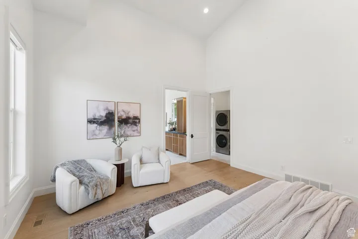 Bedroom featuring ensuite bath, high vaulted ceiling, light wood-type flooring, stacked washer / drying machine, and recessed lighting
