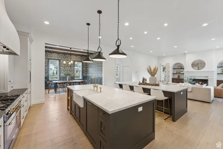 Kitchen with open floor plan, decorative light fixtures, a warm lit fireplace, light stone counters, and double oven range