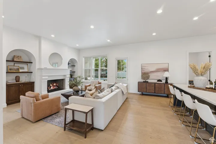 Living area with recessed lighting, light wood-style floors, a lit fireplace, and built in features