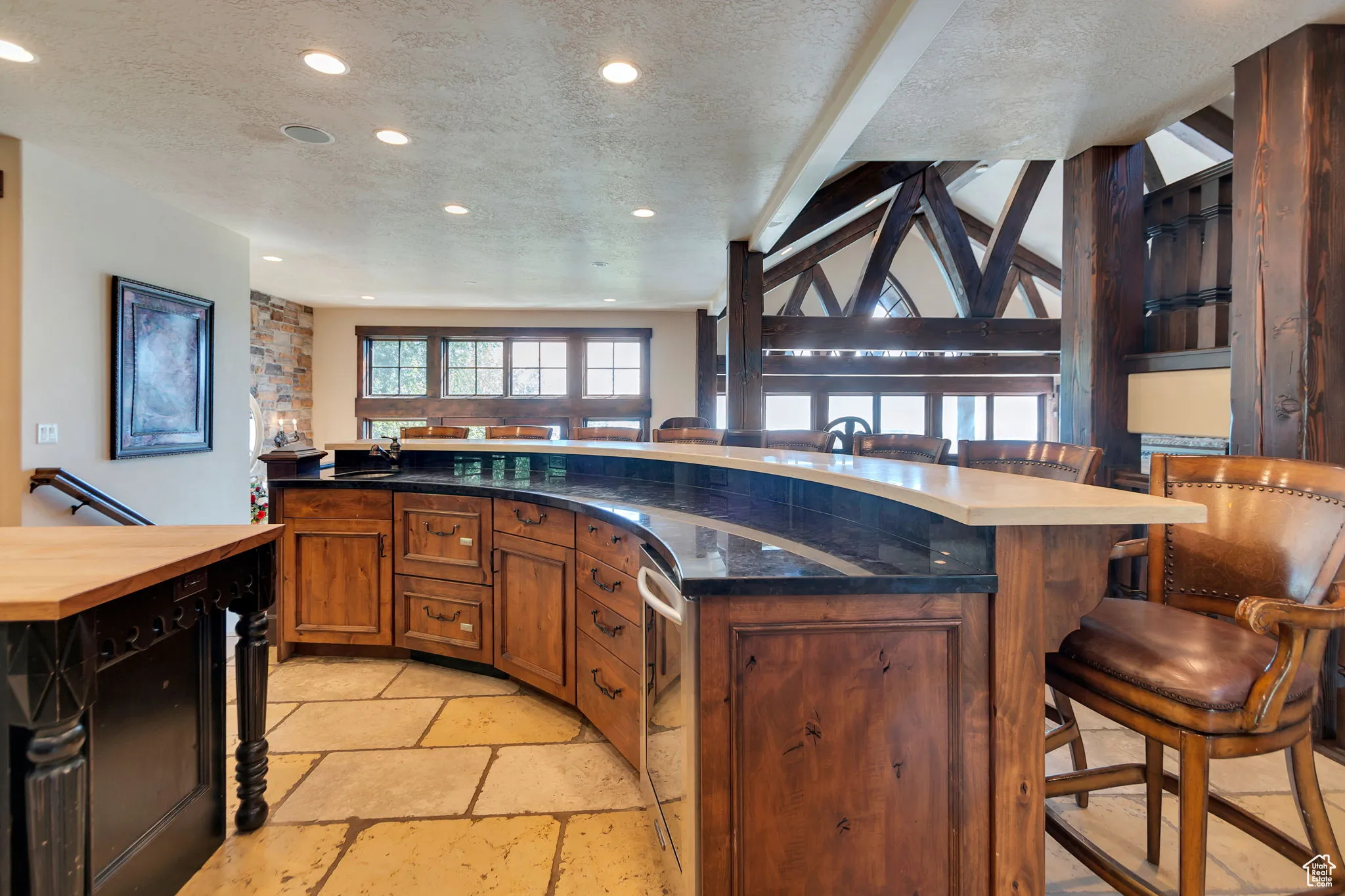 Kitchen with a breakfast bar area, a textured ceiling, open floor plan, stone tile flooring, and brown cabinets