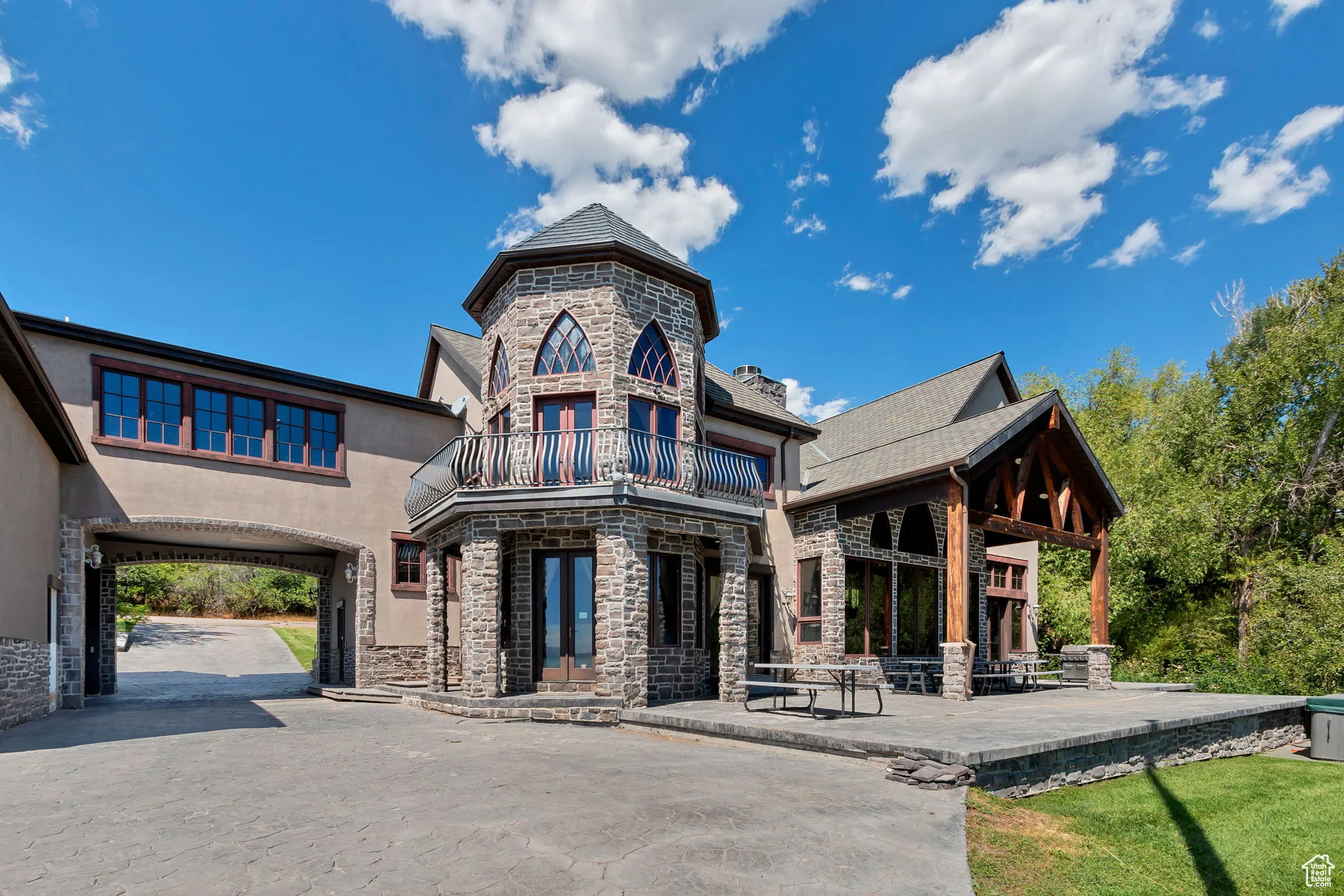 View of front of home featuring stone siding, a patio, stucco siding, and a balcony