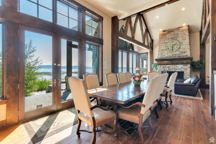 Dining space with a water view, hardwood / wood-style floors, a large fireplace, french doors, and a high ceiling