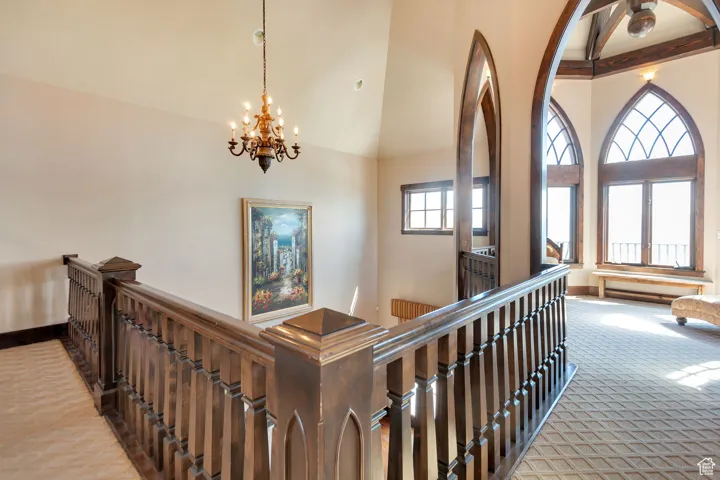 Hall featuring an upstairs landing, high vaulted ceiling, a chandelier, and carpet flooring
