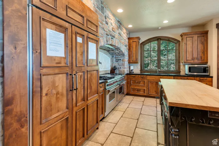 Kitchen with brown cabinets, wooden counters, stainless steel appliances, recessed lighting, and a textured ceiling