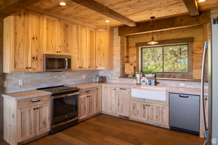 Kitchen with stainless steel appliances, light brown cabinetry, light countertops, dark wood finished floors, and a wooden ceiling with exposed beams