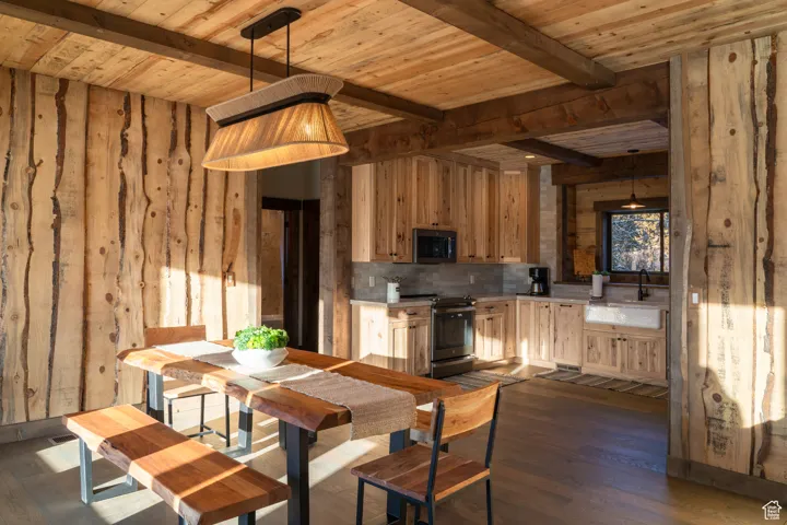 Kitchen with dark wood finished floors, decorative light fixtures, appliances with stainless steel finishes, light countertops, and a wooden ceiling with exposed beams