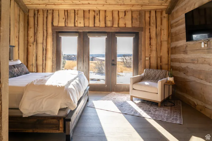 Bedroom featuring wooden walls, multiple windows, french doors, and wood finished floors