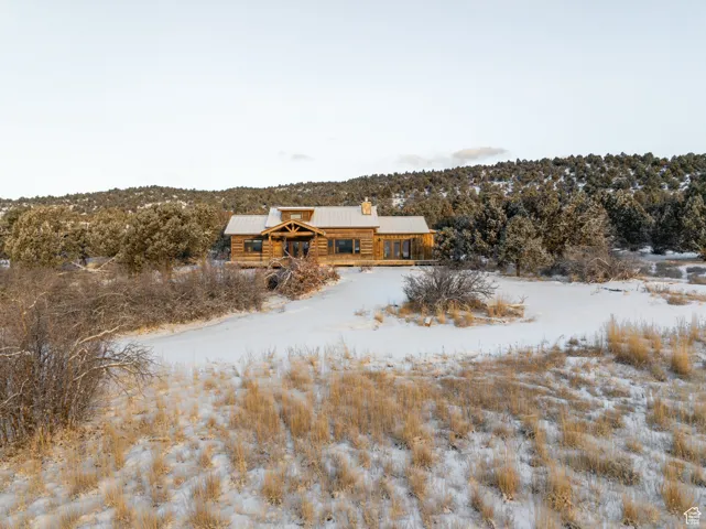 Snow covered rear of property with a metal roof, a chimney, and log siding