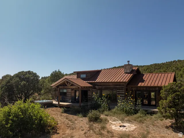 Rear view of property featuring a standing seam roof, a metal roof, a chimney, and a hot tub