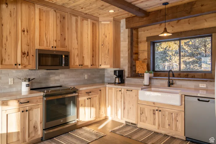 Kitchen featuring appliances with stainless steel finishes, decorative light fixtures, a wooden ceiling with exposed beams, backsplash, and light countertops