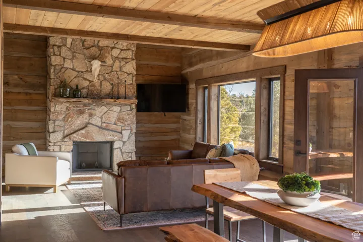 Living area with a stone fireplace, a wood ceiling with exposed beams, and hardwood / wood-style floors