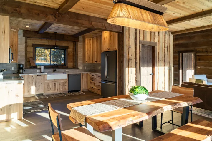 Kitchen featuring a wooden ceiling with exposed beams, dark wood-type flooring, freestanding refrigerator, black dishwasher, and wood walls