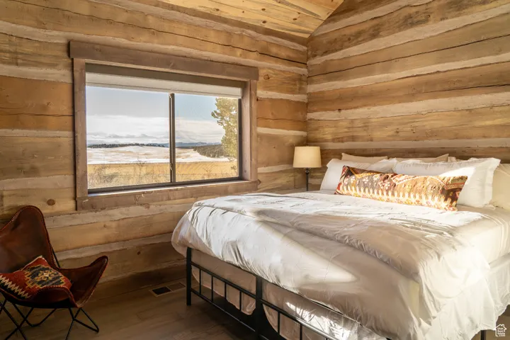 Bedroom featuring wooden walls, wood-type flooring, vaulted ceiling, and a mountain view