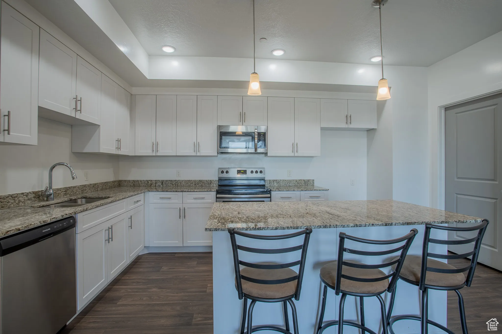 Kitchen featuring white cabinetry, appliances with stainless steel finishes, hanging light fixtures, recessed lighting, and a kitchen breakfast bar