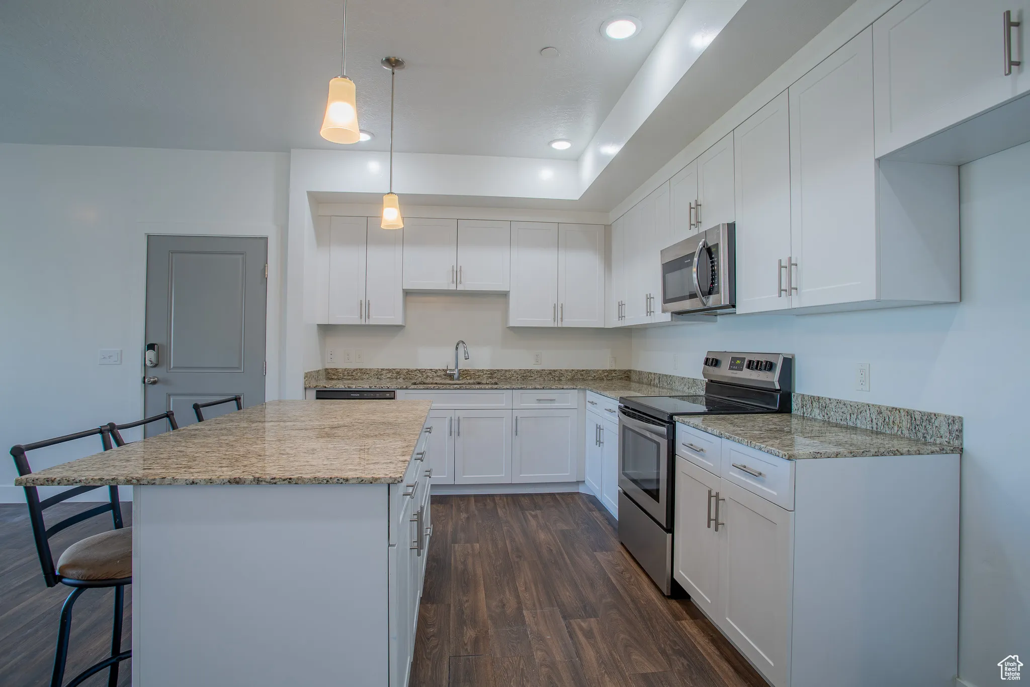 Kitchen with a kitchen bar, stainless steel appliances, dark wood-type flooring, hanging light fixtures, and white cabinetry