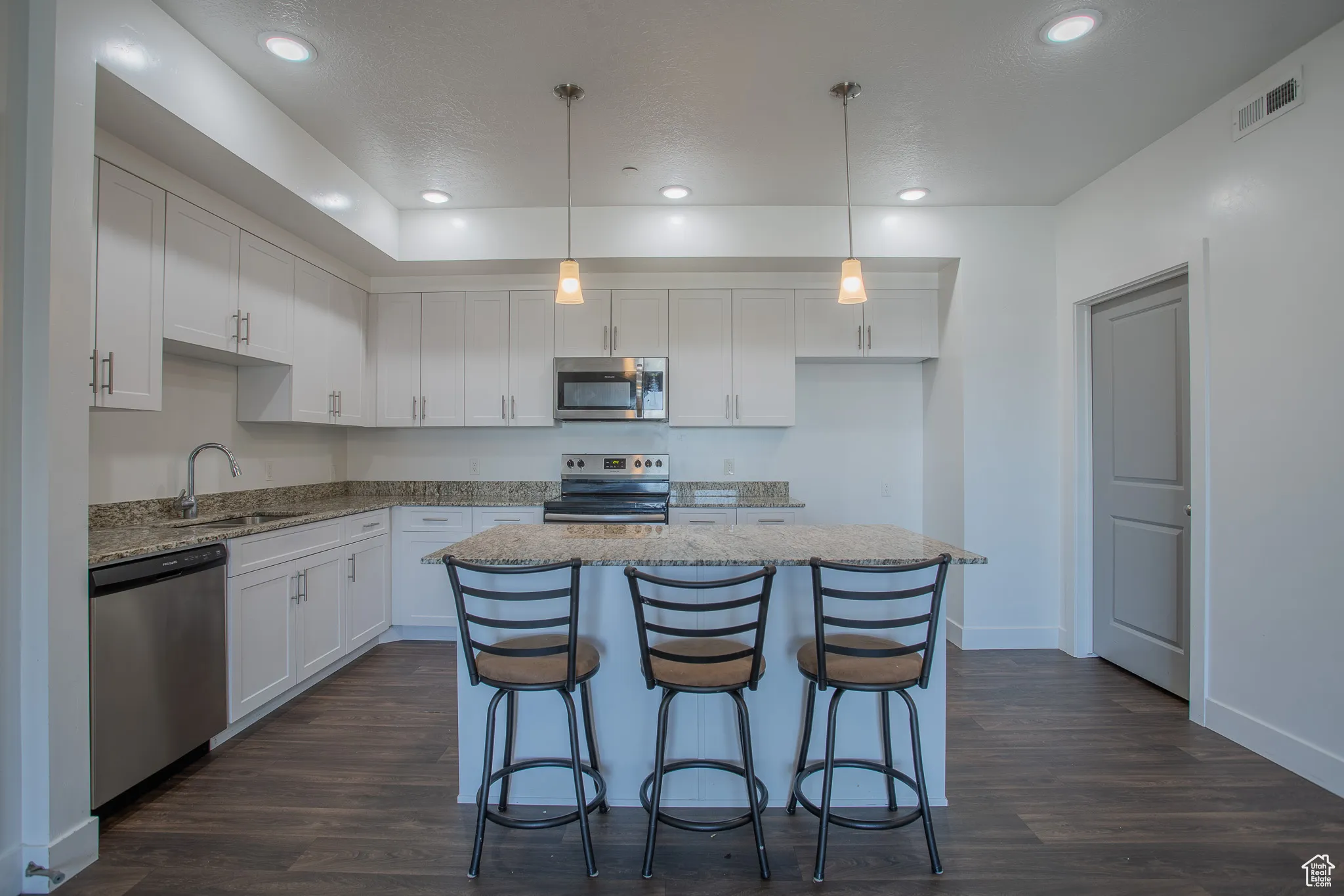 Kitchen featuring white cabinets, pendant lighting, light stone counters, and recessed lighting