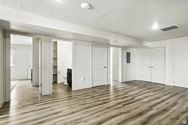 Unfurnished bedroom featuring wood finished floors, connected bathroom, a textured ceiling, electric panel, and multiple closets