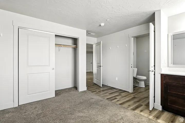Unfurnished bedroom featuring a closet, a textured ceiling, light wood-style floors, ensuite bathroom, and light colored carpet