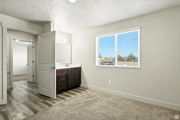 Unfurnished bedroom with a textured ceiling, light carpet, and ensuite bath