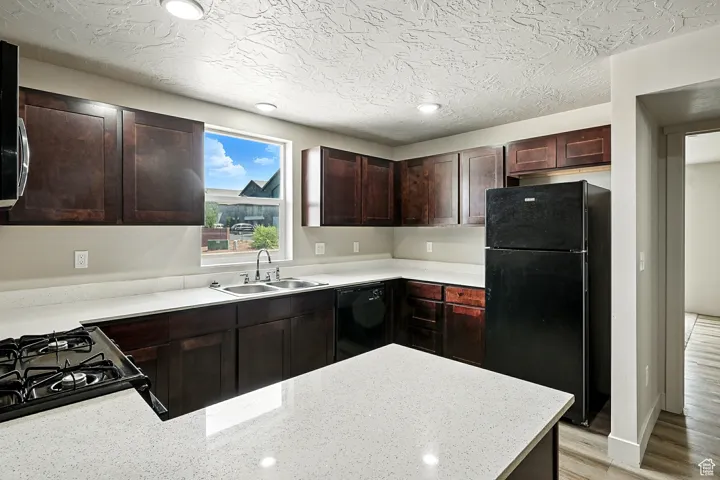 Kitchen with black appliances, dark brown cabinetry, a peninsula, light wood-style flooring, and light stone counters