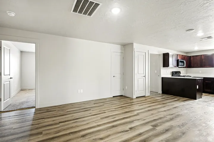 Kitchen featuring light countertops, light wood-style floors, dark brown cabinetry, a textured ceiling, and stainless steel microwave
