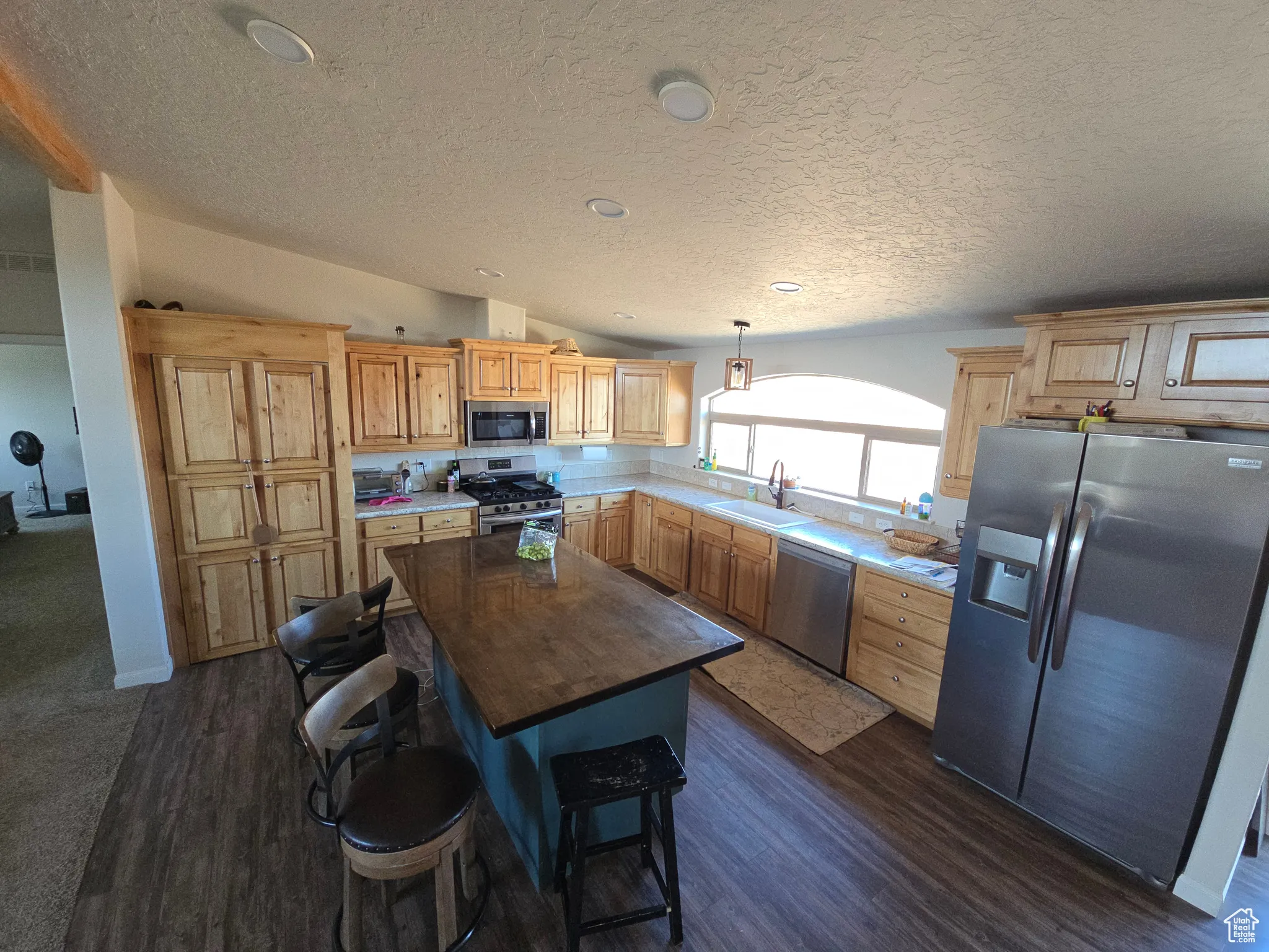 Kitchen featuring stainless steel appliances, vaulted ceiling, light brown cabinets, dark wood-style floors, and a textured ceiling