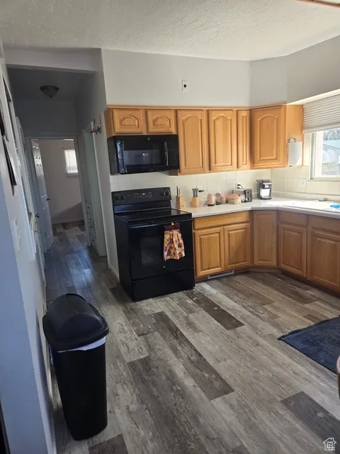 Kitchen featuring black appliances, decorative backsplash, dark wood finished floors, light countertops, and brown cabinetry