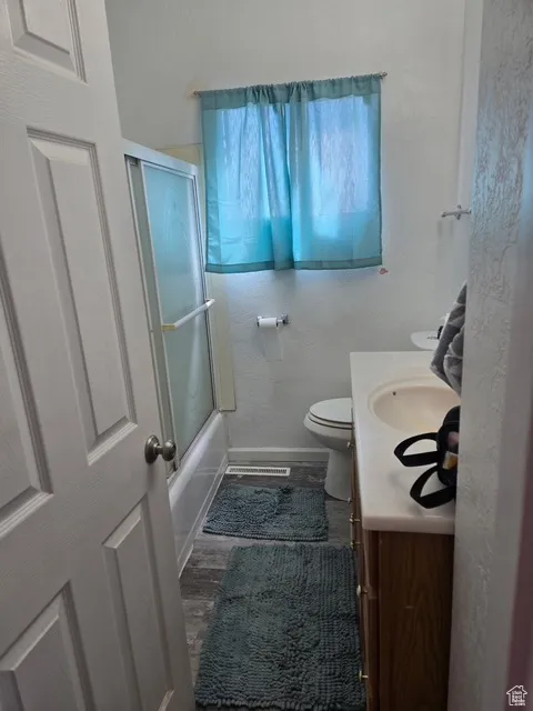 Full bathroom featuring vanity, combined bath / shower with glass door, and a textured wall