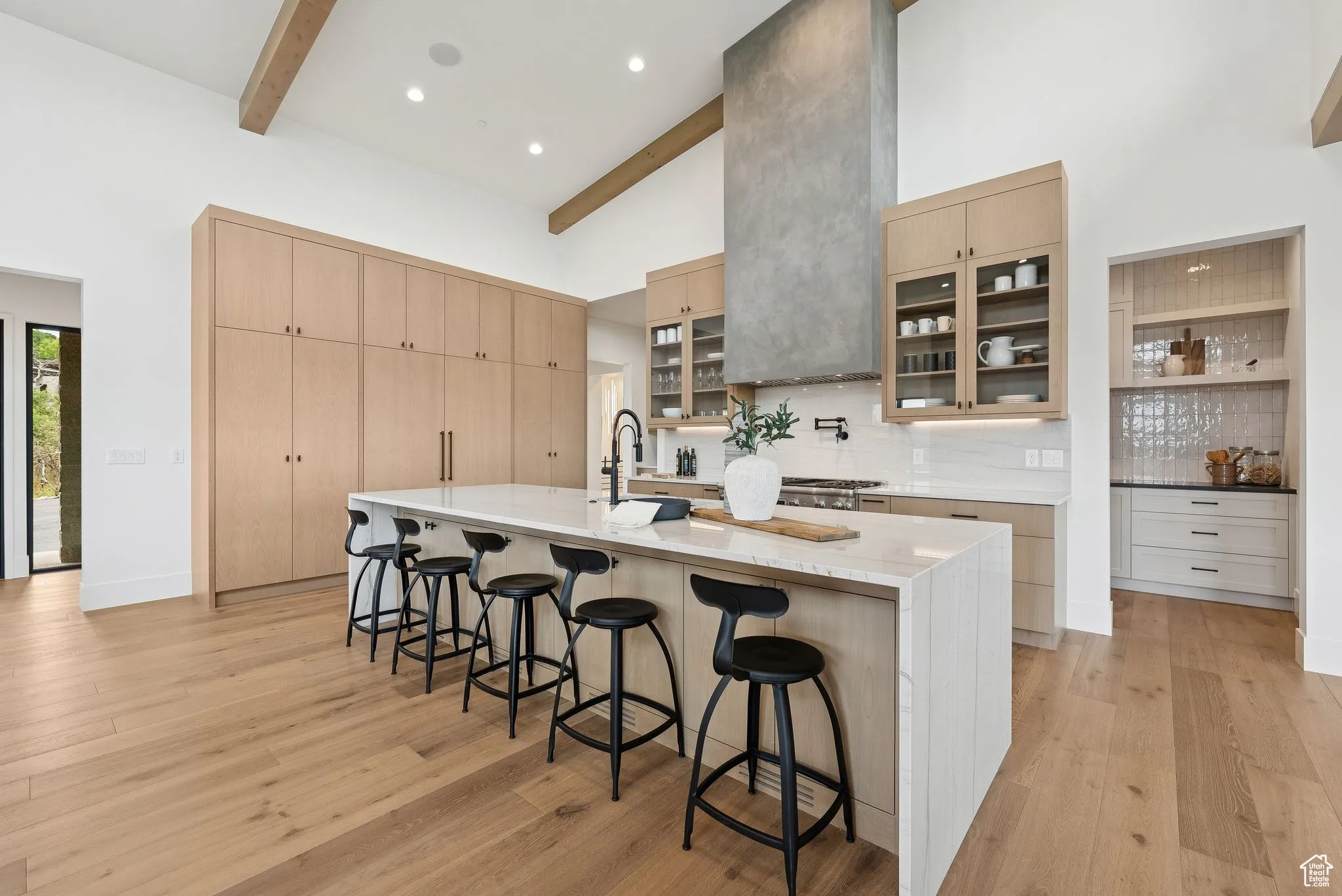 Kitchen with glass insert cabinets, a kitchen bar, light brown cabinets, high vaulted ceiling, and backsplash