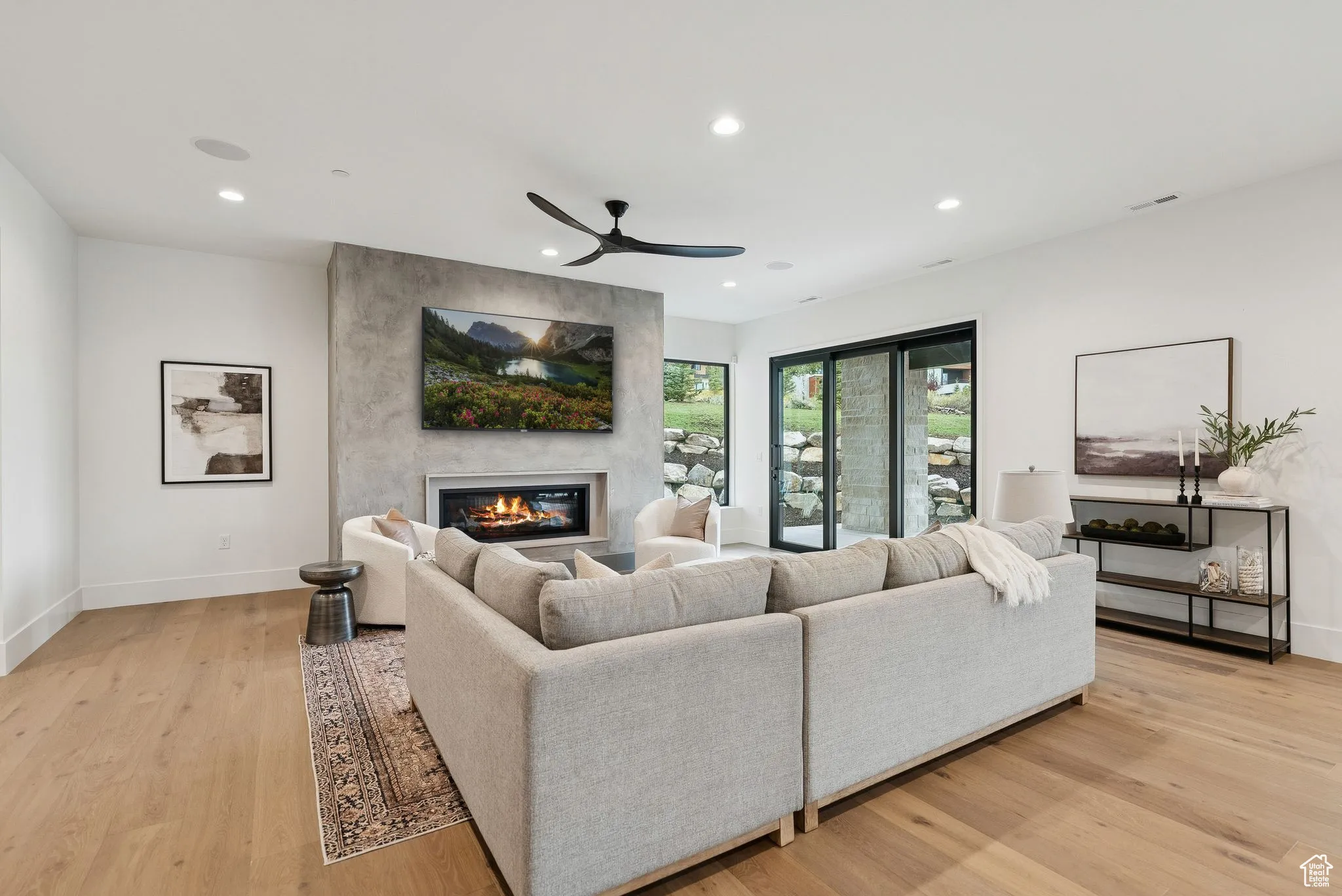Living area with a glass covered fireplace, recessed lighting, light wood-type flooring, and a ceiling fan