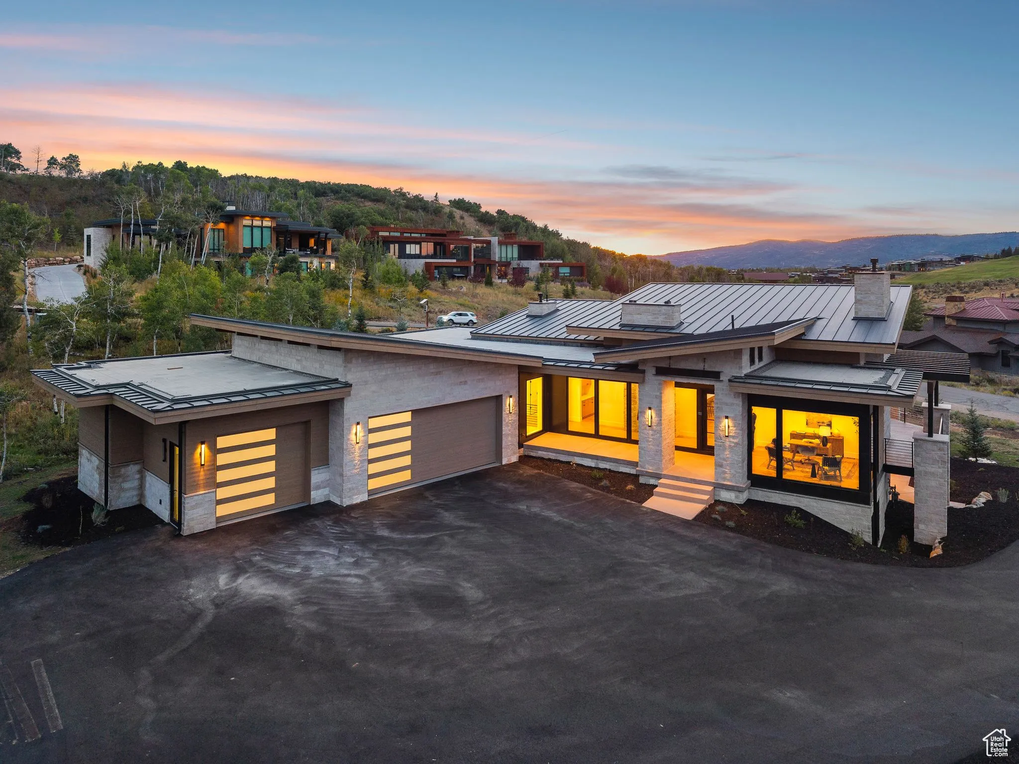 Contemporary home featuring a standing seam roof, a garage, a metal roof, stone siding, and driveway