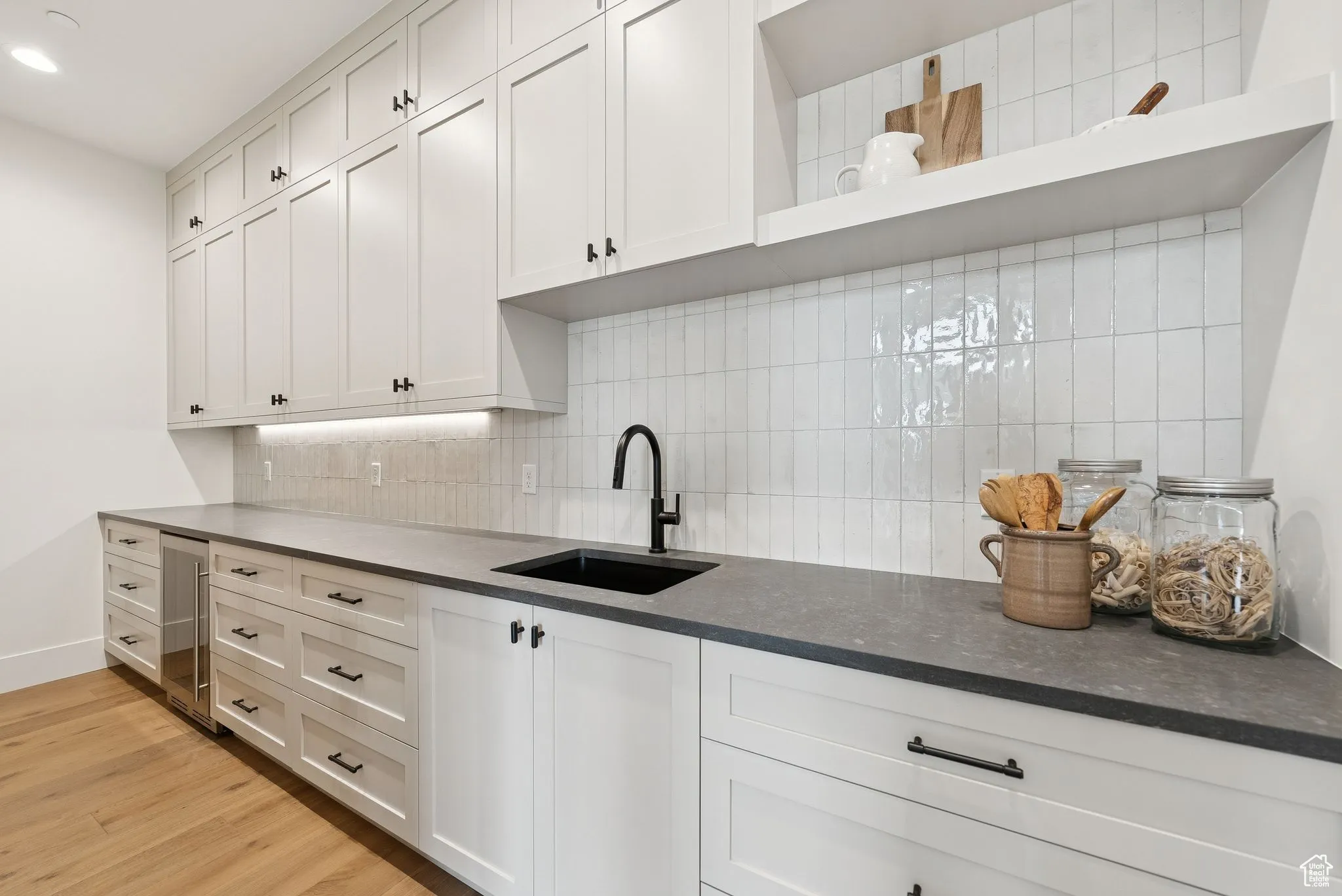 Kitchen featuring open shelves, light wood-style floors, tasteful backsplash, white cabinetry, and beverage cooler