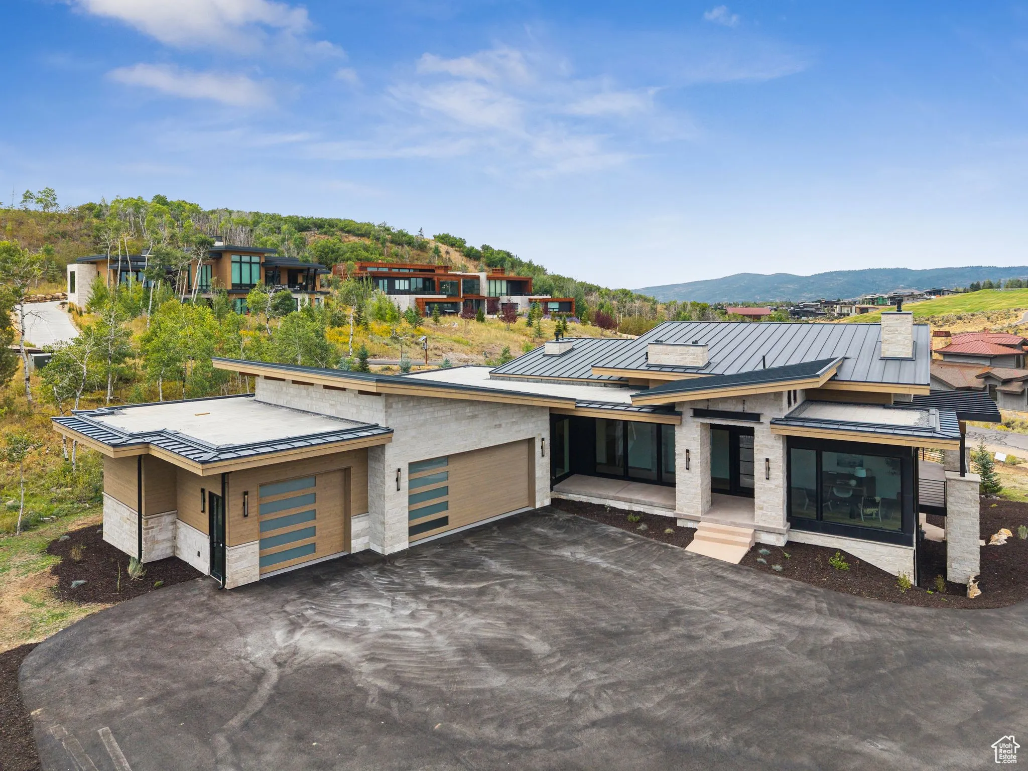 Contemporary house featuring a standing seam roof, driveway, a metal roof, stone siding, and a garage