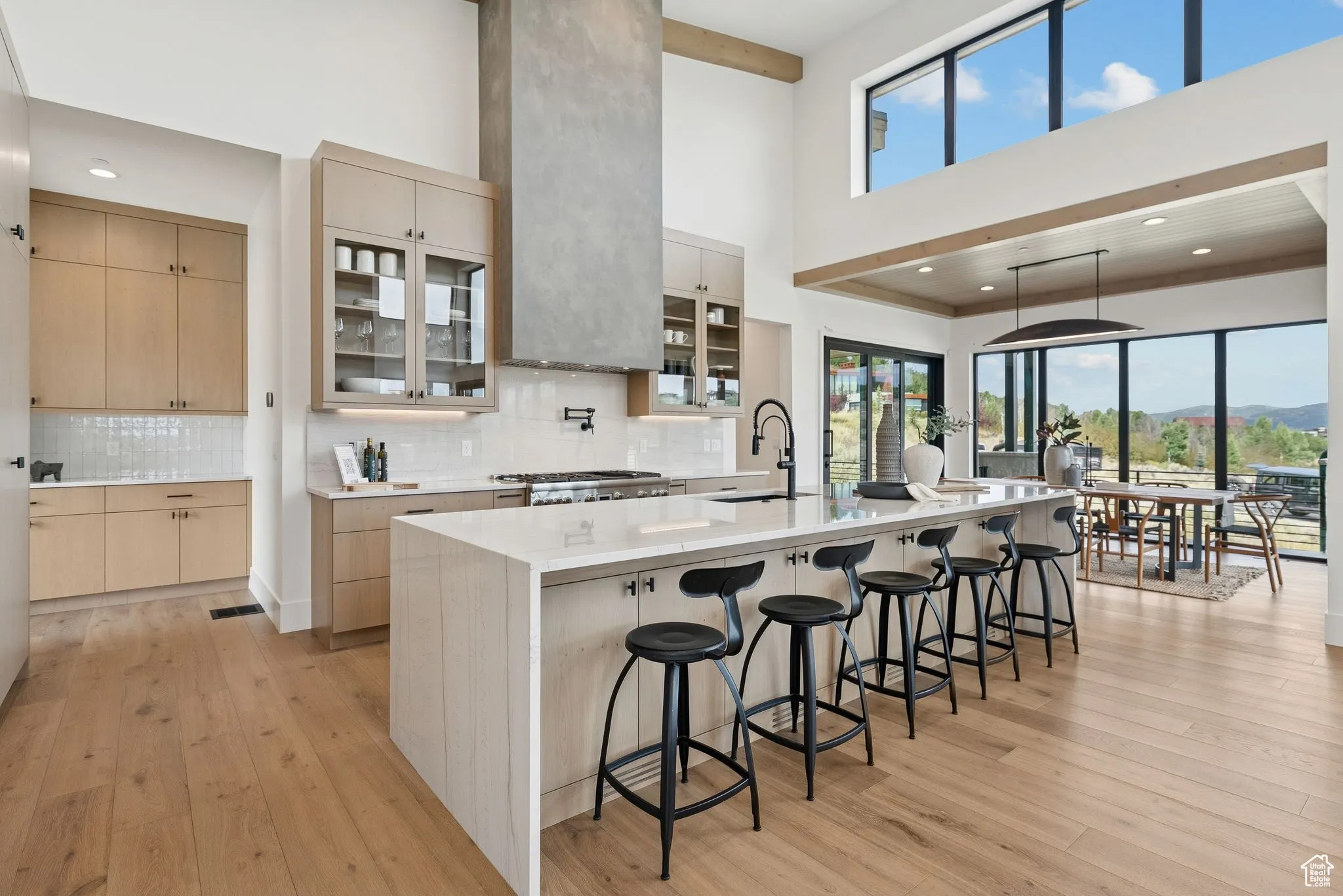 Kitchen featuring glass insert cabinets, a kitchen breakfast bar, light brown cabinets, light wood finished floors, and a high ceiling