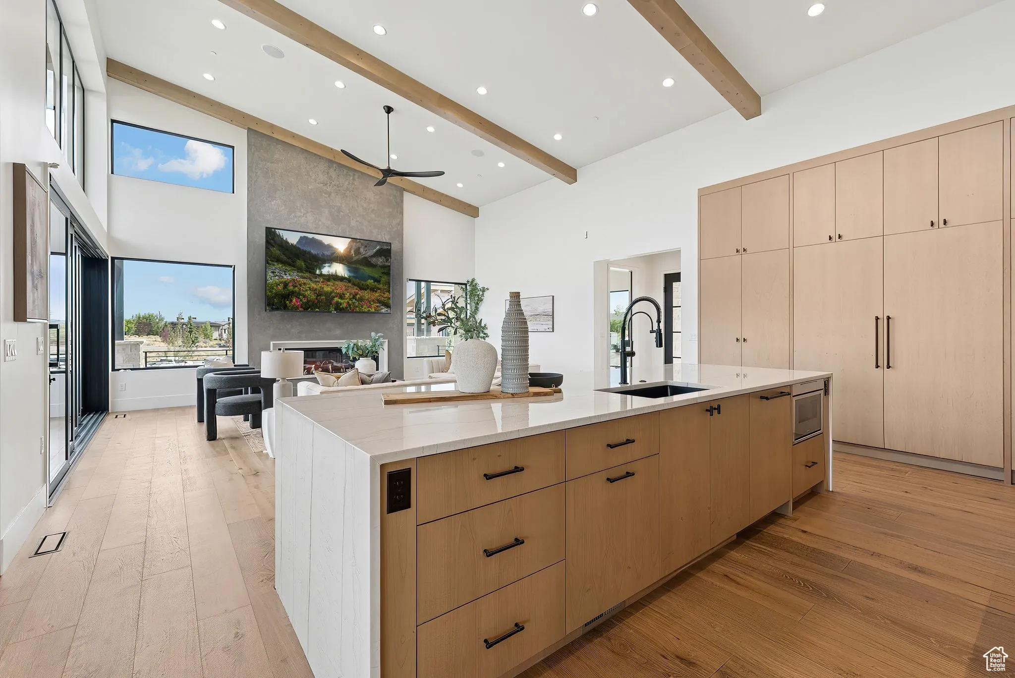Kitchen featuring light brown cabinets, light wood-type flooring, light stone countertops, a ceiling fan, and a large fireplace