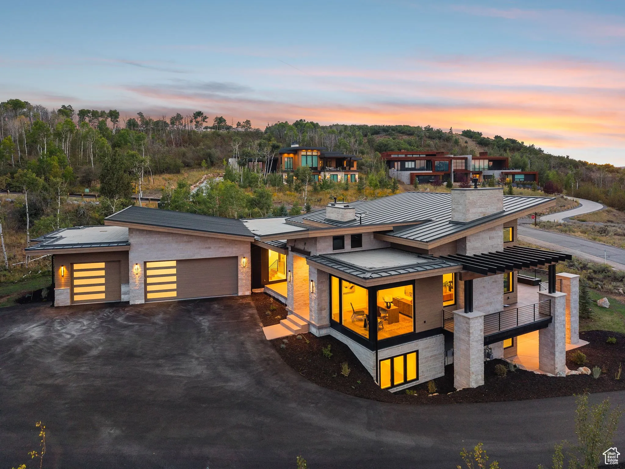 Modern home featuring a standing seam roof, driveway, an attached garage, a metal roof, and stone siding